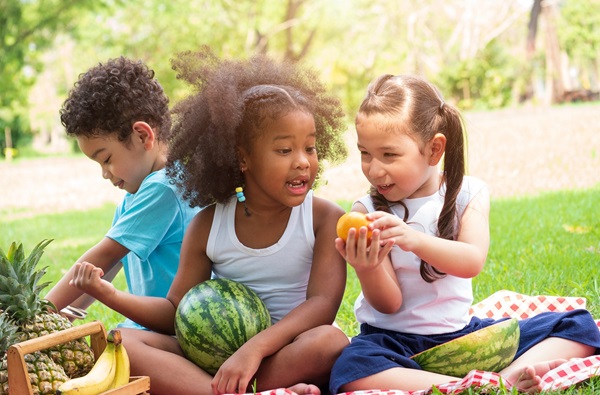 Drie kinderen buiten aan het picknicken met fruit