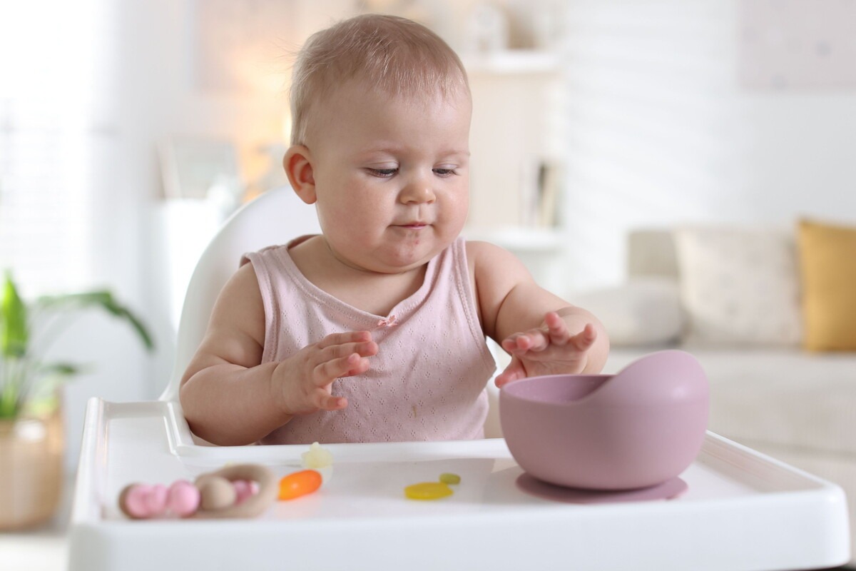 Baby zit in een kinderstoel en heeft een bakje met eten voor zich