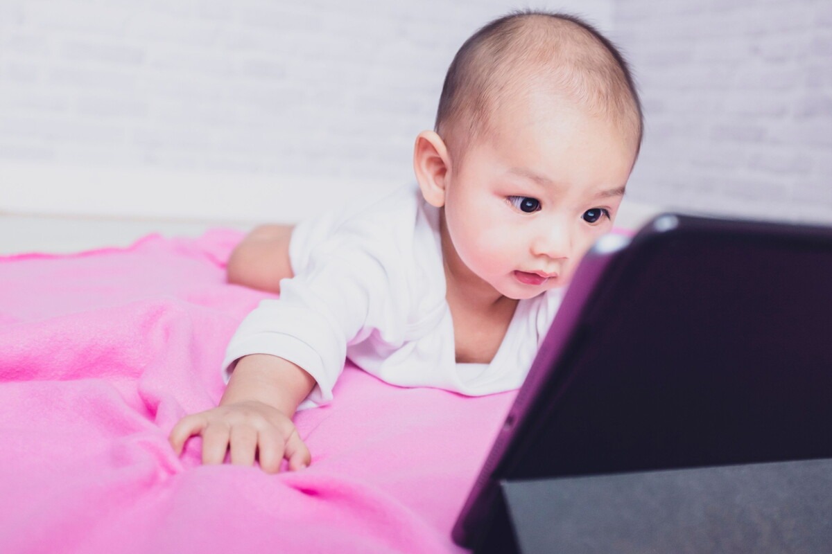 Een baby ligt op zijn buik en kijkt een filmpje op een tablet