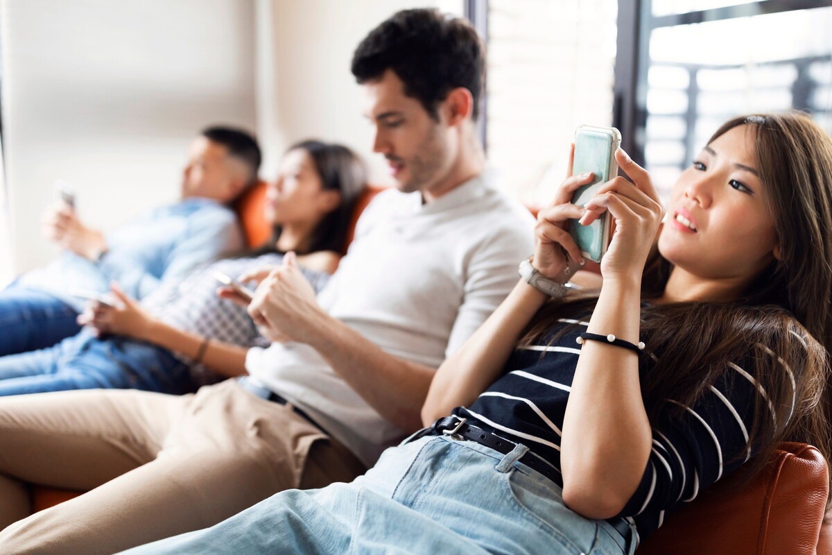 Een groep jongeren zit op de bank naast elkaar en kijken allemaal op hun telefoon