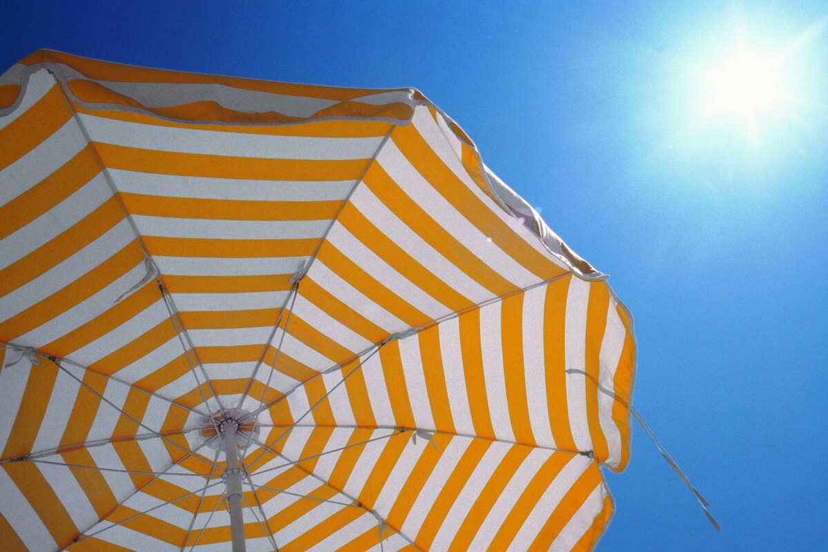 Wit oranje gestreepte parasol met een blauwe lucht en felle zon