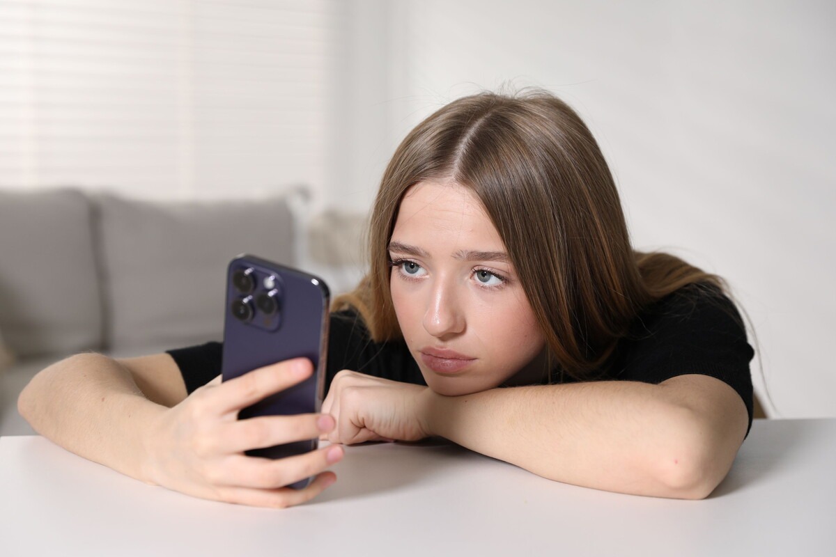 Tiener meisje kijkt verveeld op haar mobiele telefoon
