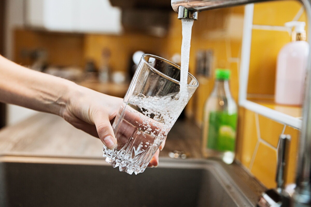 Iemand houdt een glas onder de kraan en vult hem met water