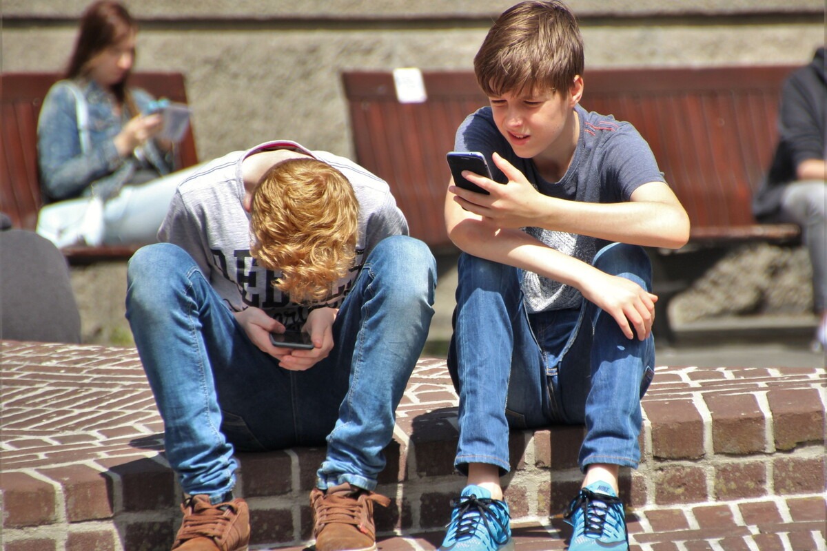 Twee jongens zitten buiten op straat en kijken op hun mobiele telefoon