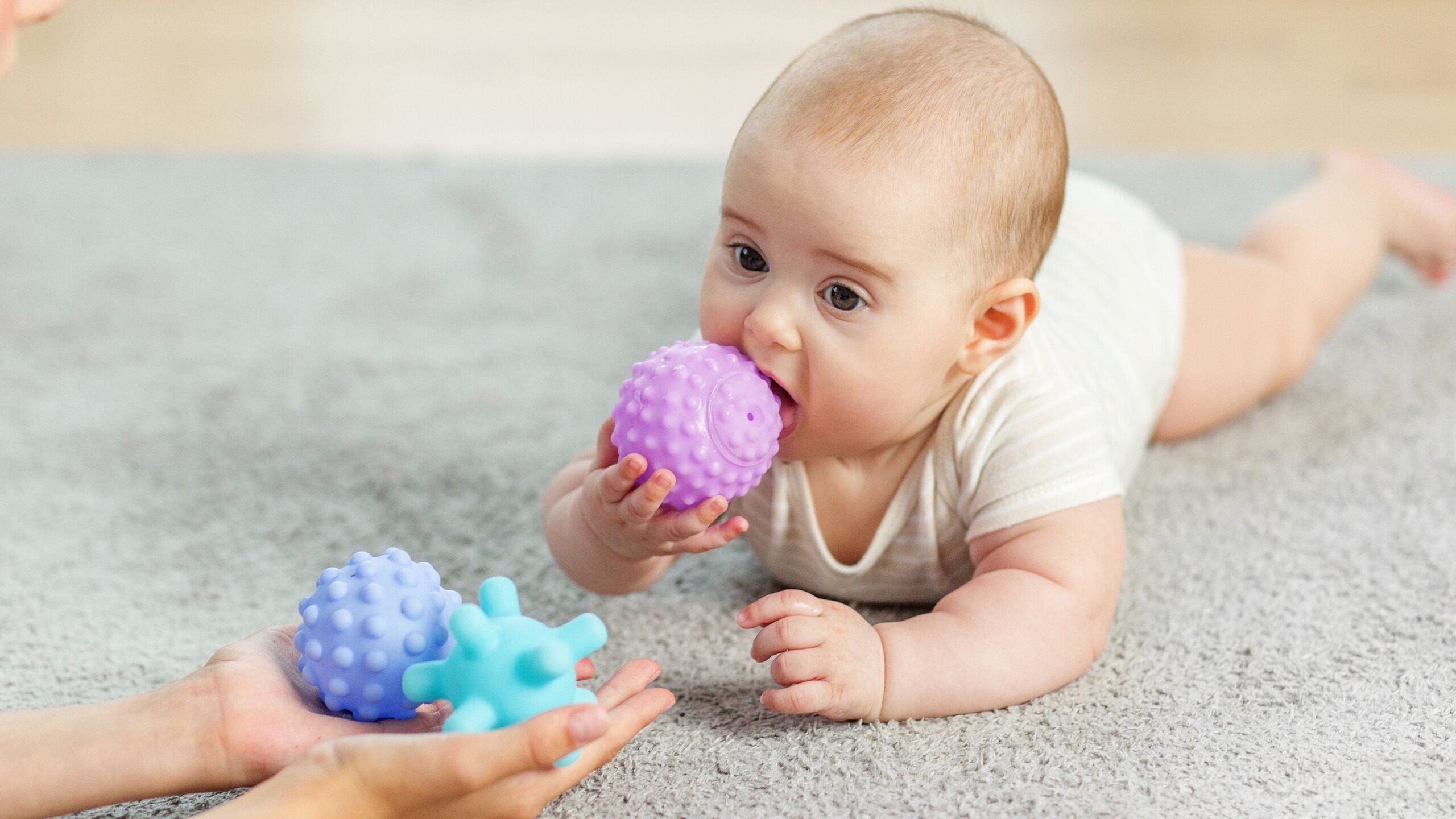 Baby ligt op buik en stopt een speeltje in zijn mond