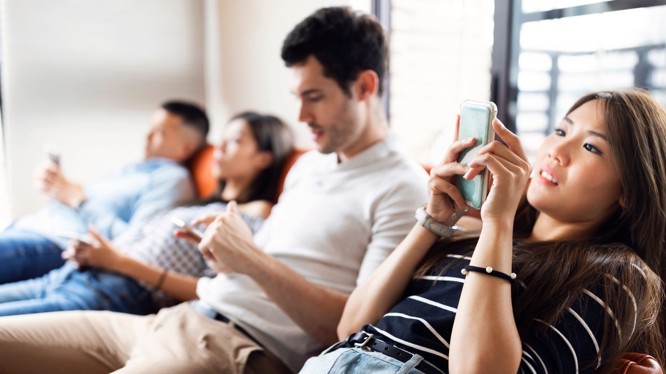 Een groep jongeren zit op de bank naast elkaar en kijken allemaal op hun telefoon