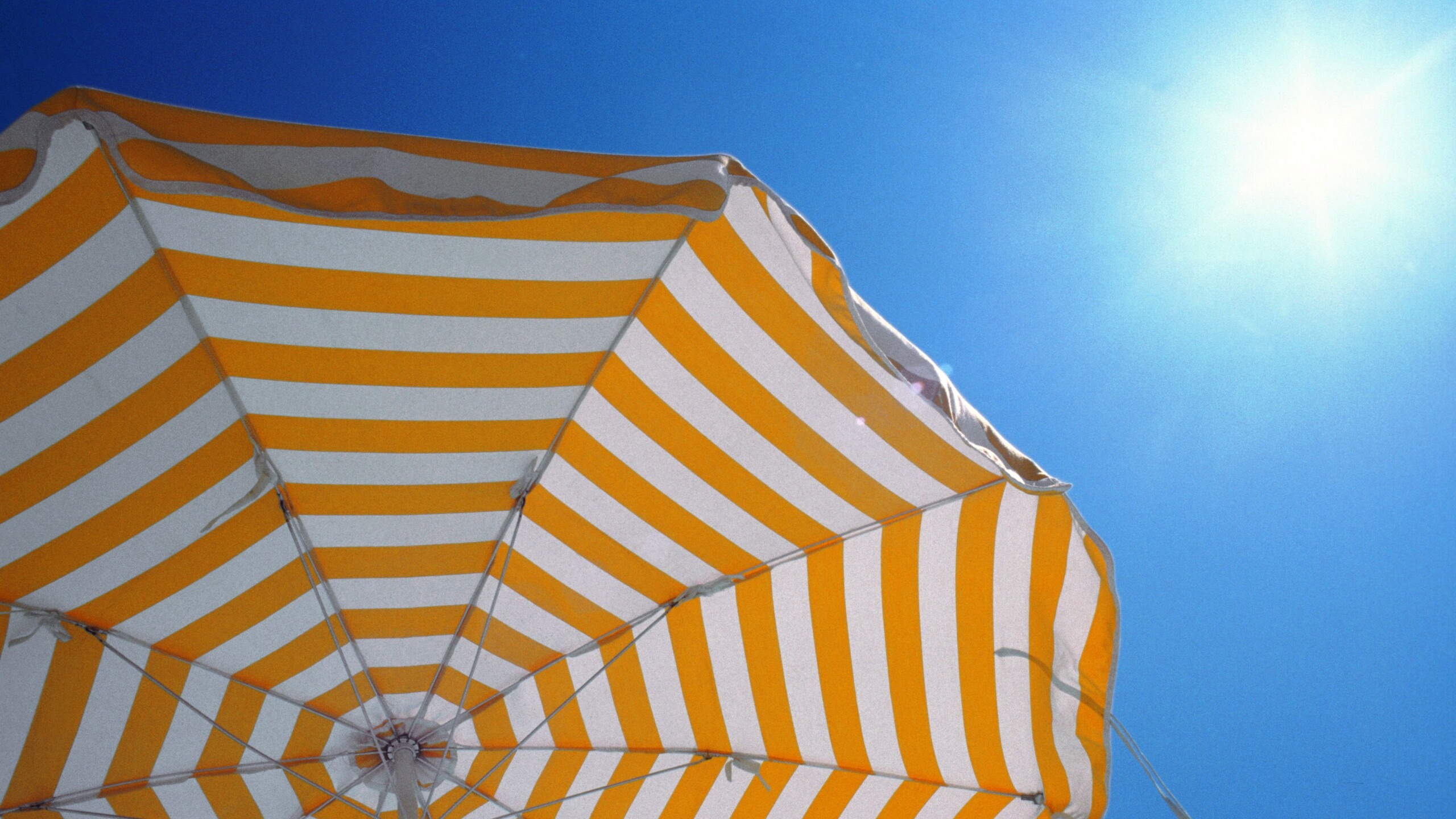 Wit oranje gestreepte parasol met een blauwe lucht en felle zon