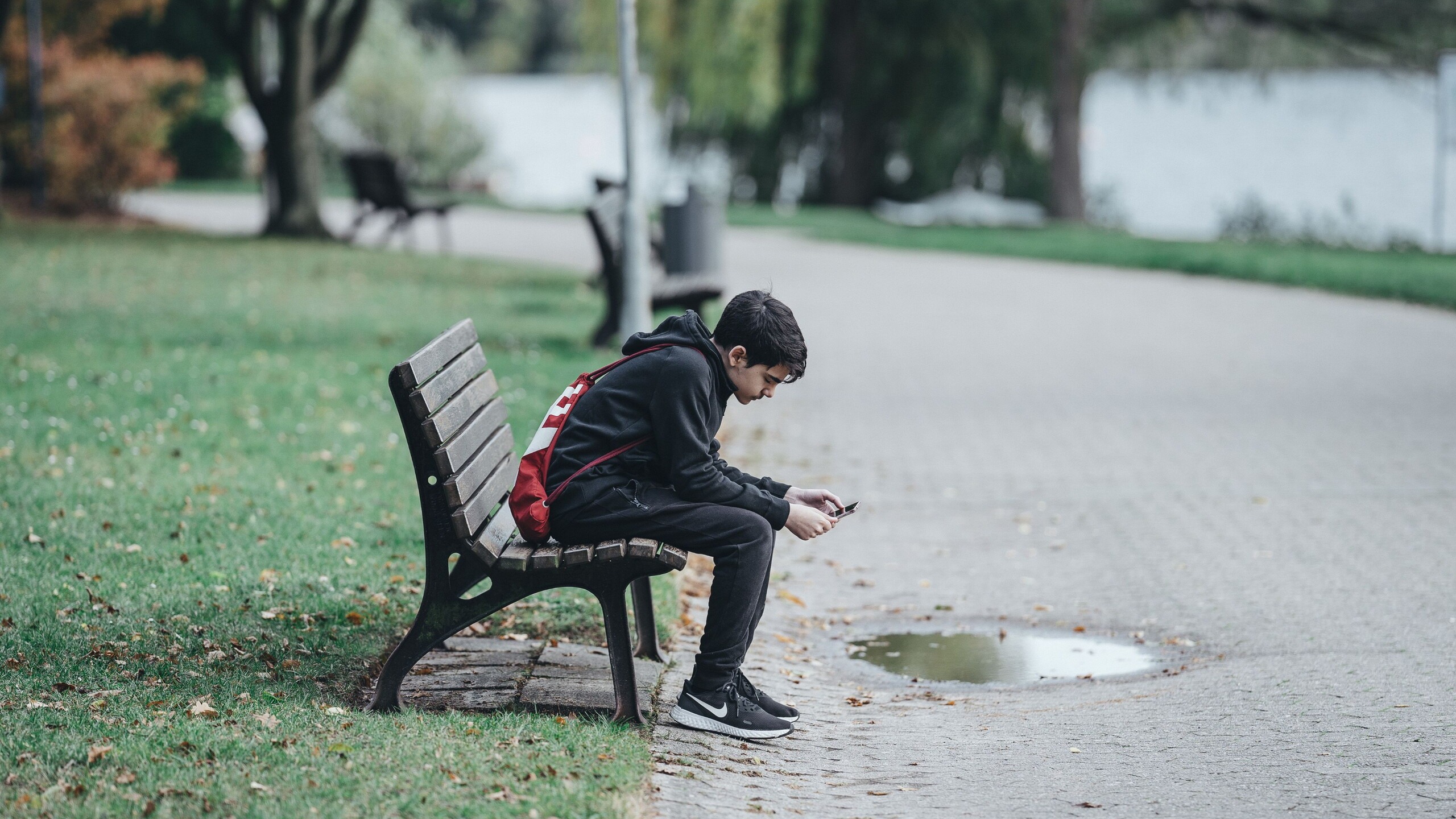Een tiener zit op een bankje in het park en lijkt depressief