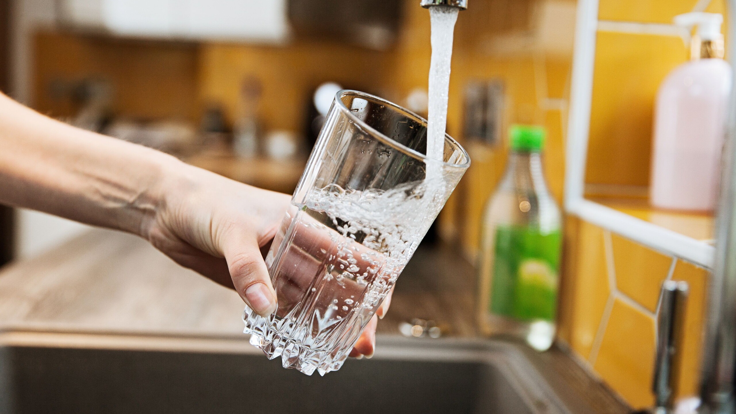 Iemand houdt een glas onder de kraan en vult hem met water