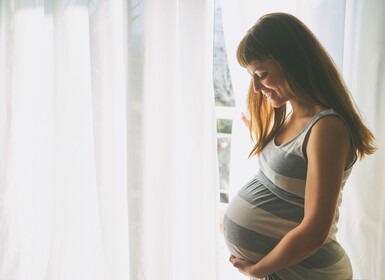 Zwangere vrouw staat voor het raam en kijkt naar haar buik